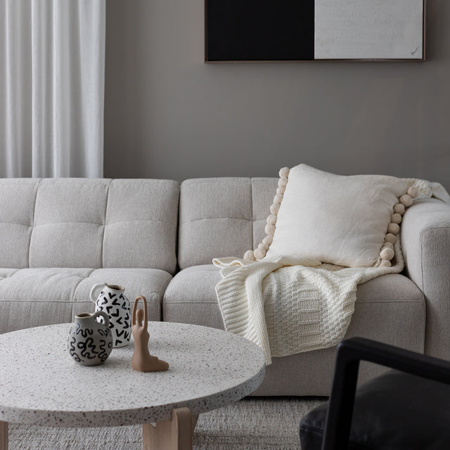 Canape beige clair matelasse avec coussin et plaid creme, table basse ronde en terrazzo.