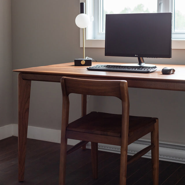 Bureau en bois noyer avec ordinateur, clavier et lampe moderne dans espace de travail.