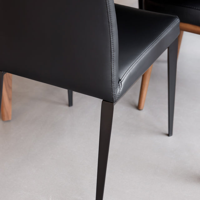 Chaise de salle à manger en cuir noire avec pieds fins, placée autour d’une table en bois massif moderne.