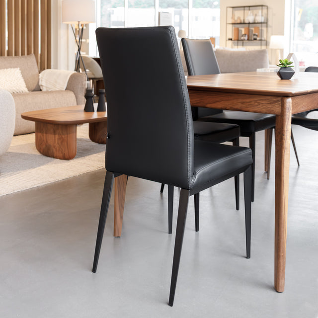 Chaise de salle à manger en cuir noire avec pieds fins, placée autour d’une table en bois massif moderne.