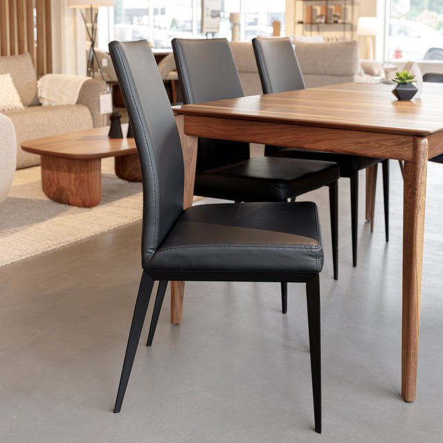 Chaise de salle à manger en cuir noire avec pieds fins, placée autour d’une table en bois massif moderne.