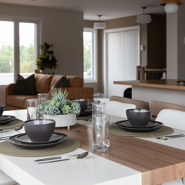 table de salle a manger en bois et resine blanche, dressee avec vaisselle noire, verres transparents et plante decorative au centre.