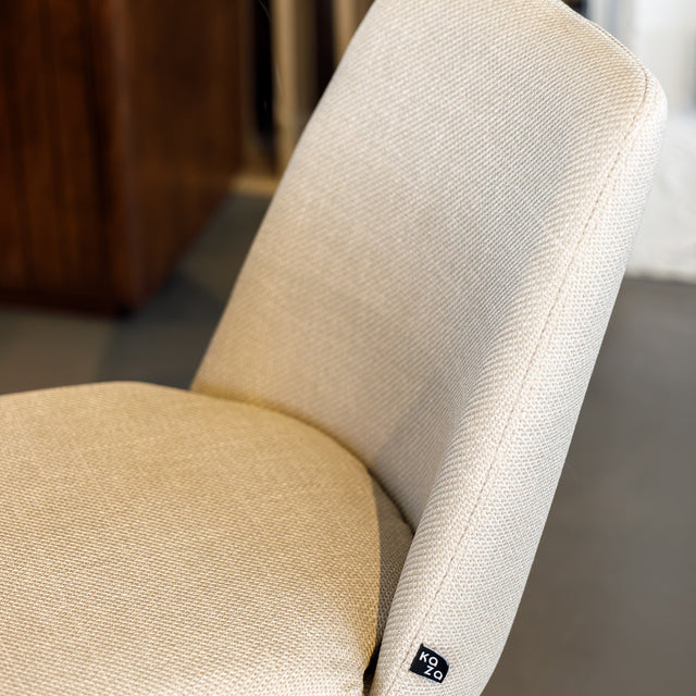 Chaise de salle à manger en tissu beige avec piètement noirs, placée près d’une table en bois dans un intérieur moderne.