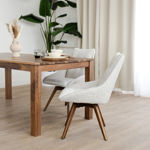 Chaise de salle à manger en tissu truffle sauvage avec piétement en bois noyer, placée près d’une table en bois moderne.