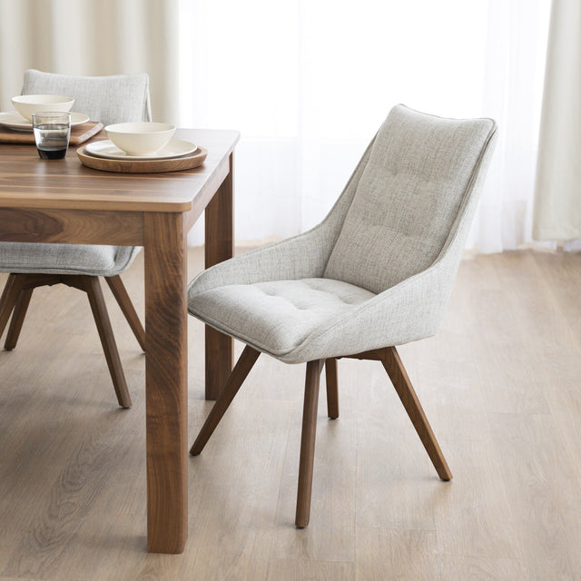 Chaise de salle à manger en tissu truffle sauvage avec piétement en bois noyer, placée près d’une table en bois moderne.