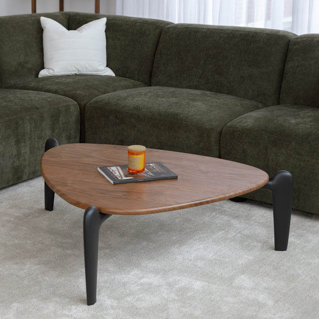Table basse triangulaire en bois avec pieds noirs, au design contemporain dans un salon lumineux.