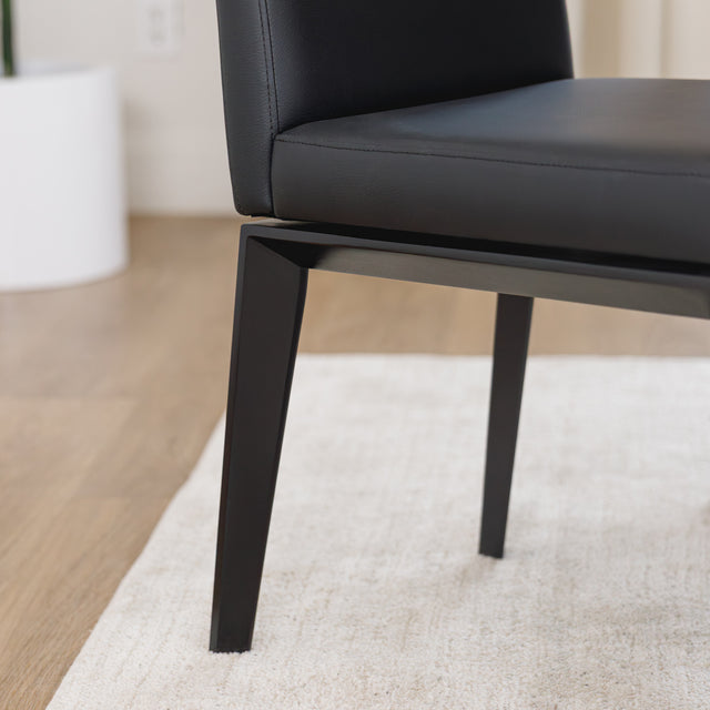 Chaise de cuisine en cuir végane noir avec pieds assortis autour d’une table en bois moderne.