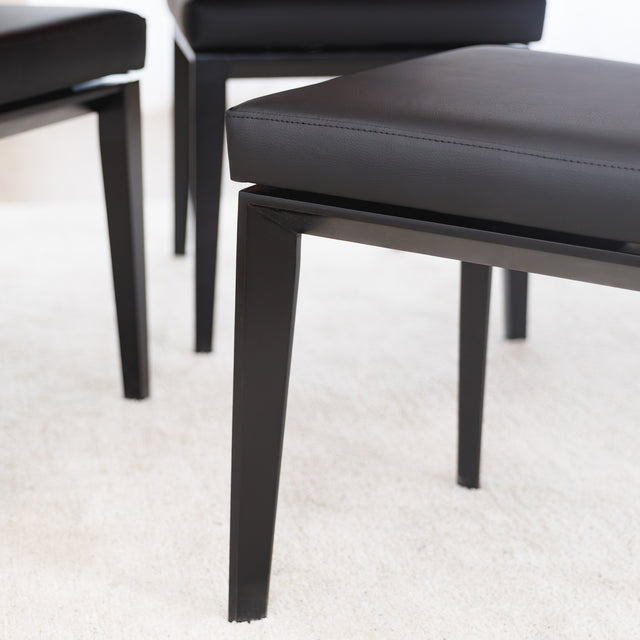 Chaise de cuisine en cuir végane noir avec pieds assortis autour d’une table en bois moderne.
