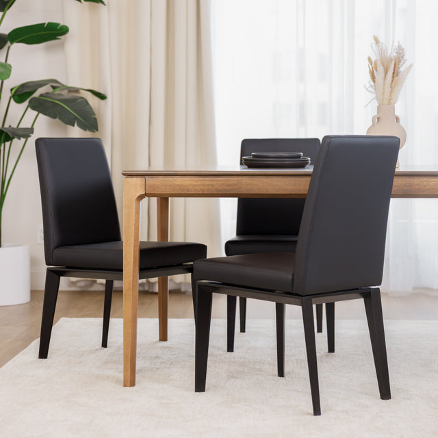 Chaise de cuisine en cuir végane noir avec pieds assortis autour d’une table en bois moderne.