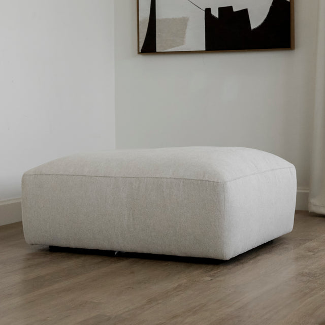 pouf rectangulaire beige clair en tissu sur sol en bois clair.