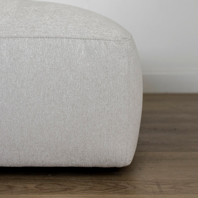 detail du bord inferieur d un pouf beige clair en tissu sur sol en bois.