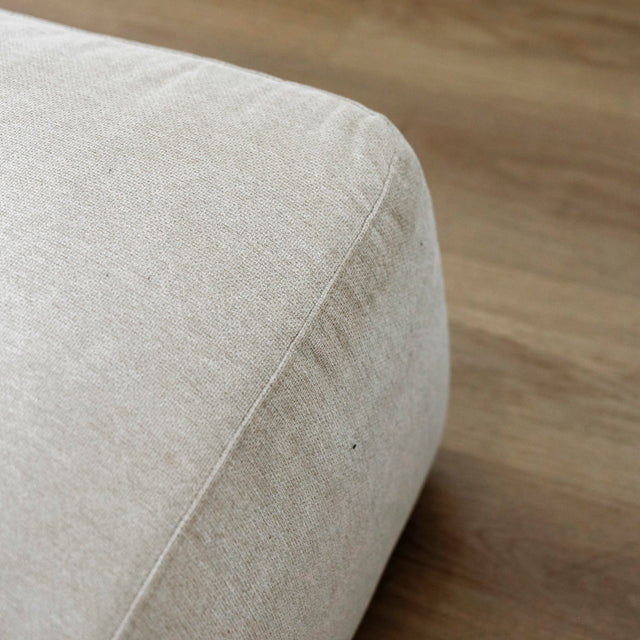 detail du bord inferieur d un pouf beige clair en tissu sur sol en bois.