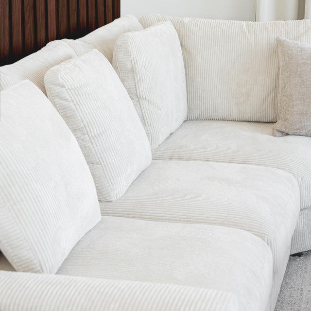 Modulaire d angle en tissu corduroy creme avec table basse en bois et decor minimaliste sur tapis clair.