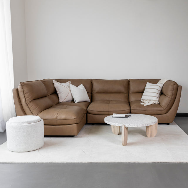 canape d angle en cuir brun clair avec coussins beiges sur tapis creme.