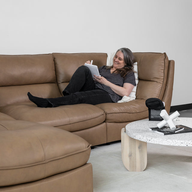 canape en cuir brun clair avec personne lisant appuyee sur coussin blanc.