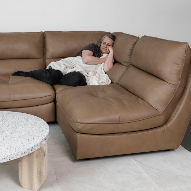 canape d angle en cuir brun clair avec personne allongee et plaid beige.