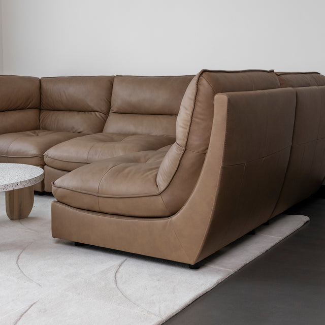 canape d angle en cuir brun clair avec assises capitonnees et lignes courbees.