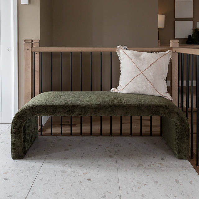 Banc en velours vert olive avec coussin beige a franges dans un interieur moderne.