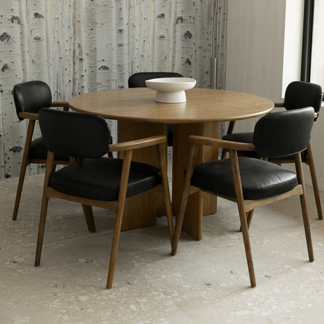 table ronde en bois avec chaises noires en cuir et accoudoirs en bois.