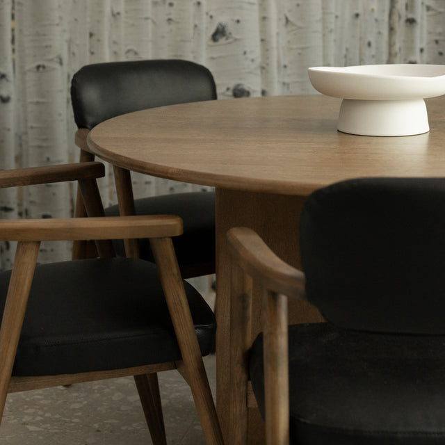 table ronde en bois avec chaises noires a accoudoirs en bois clair.