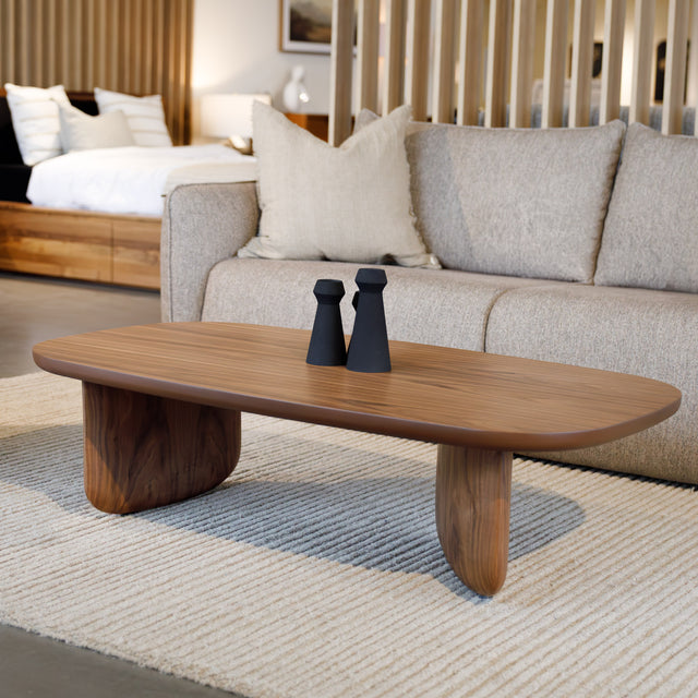 Table basse ovale en bois noyer dans un salon moderne avec un canapé beige.