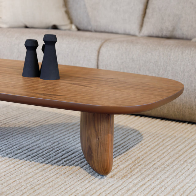 Table basse ovale en bois noyer dans un salon moderne avec un canapé beige.
