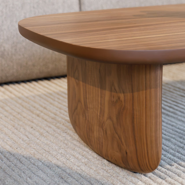 Table basse ovale en bois noyer dans un salon moderne avec un canapé beige.