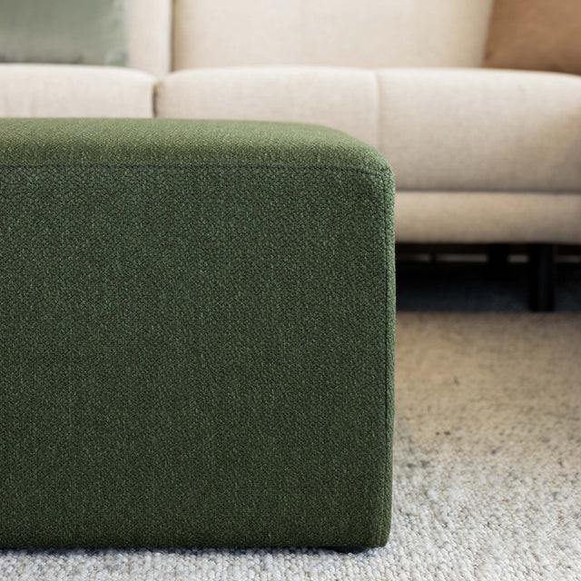 Détail ottoman carré vert en tissu texturé, finition soignée et angle net pour salon moderne.