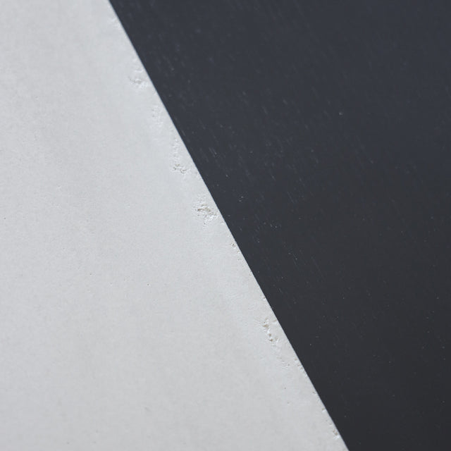 Table à manger moderne avec plateau béton ciment, tranche de frêne noir et piètement en métal noir, idéale pour salle à manger contemporaine.