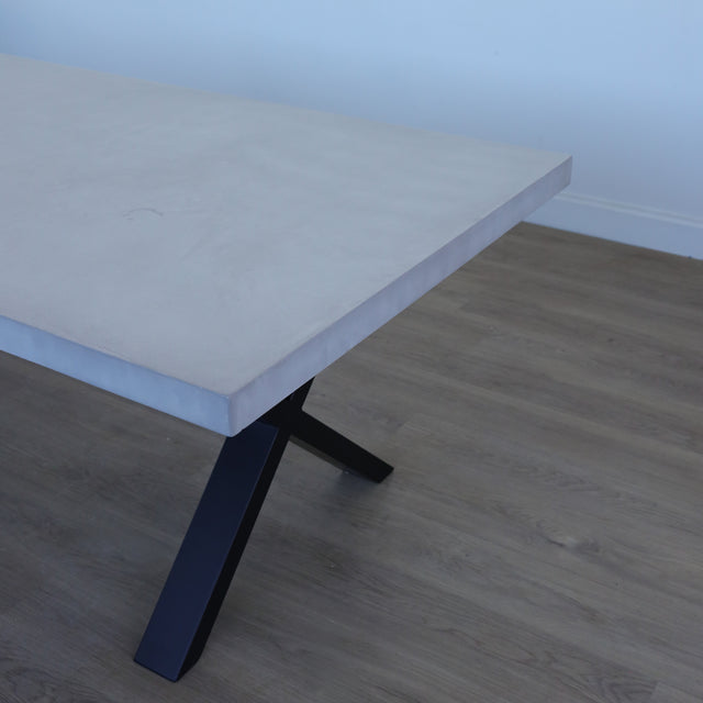 Table de salle à manger au design rectangulaire, plateau clair et piétement en X noirs, dans une salle à manger lumineuse.