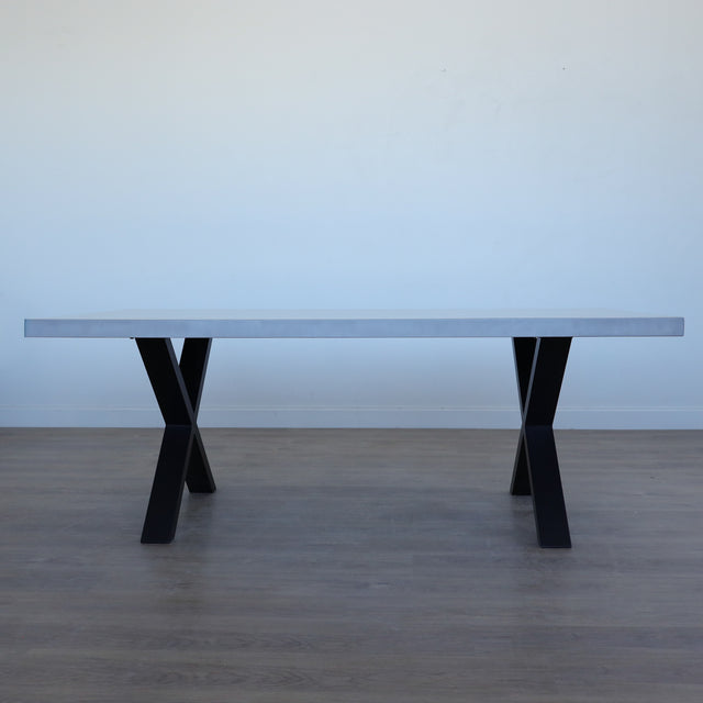 Table de salle à manger au design rectangulaire, plateau clair et piétement en X noirs, dans une salle à manger lumineuse.