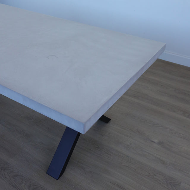 Table de salle à manger au design rectangulaire, plateau clair et piétement en X noirs, dans une salle à manger lumineuse.