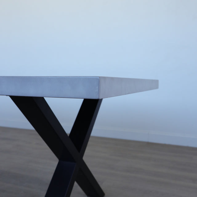 Table de salle à manger au design rectangulaire, plateau clair et piétement en X noirs, dans une salle à manger lumineuse.