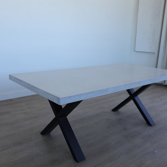 Table de salle à manger au design rectangulaire, plateau clair et piétement en X noirs, dans une salle à manger lumineuse.