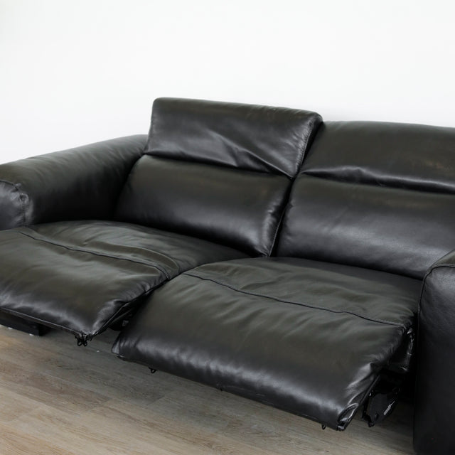 canape relax en cuir noir avec dossiers inclinables et repose pieds ouverts sur parquet clair.