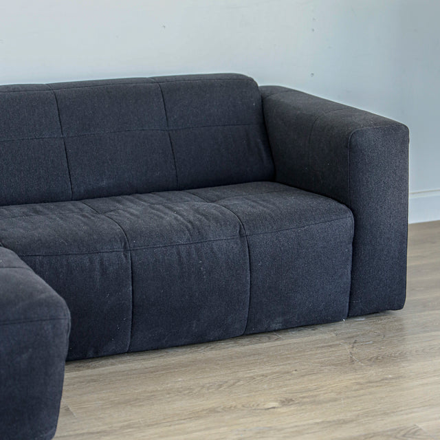 Canape gris fonce matelasse avec accoudoir large et design contemporain.