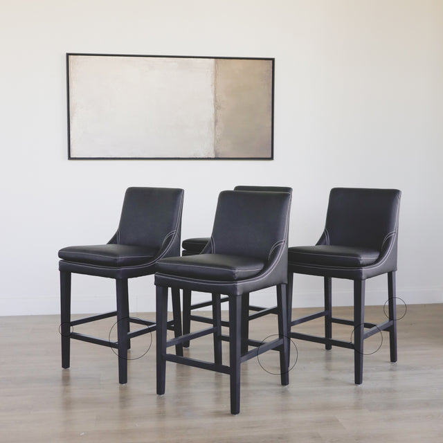 ensemble de tabourets comptoir en cuir végane noir avec coutures blanches et pieds en bois sombre avec des cercles indiquant les défauts.