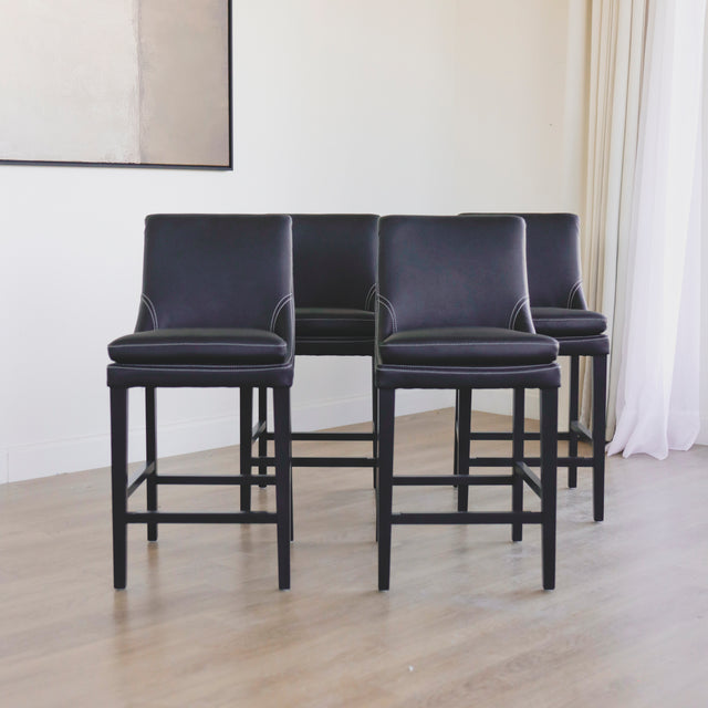 ensemble de tabourets comptoir en cuir végane noir avec coutures blanches et pieds en bois sombre.