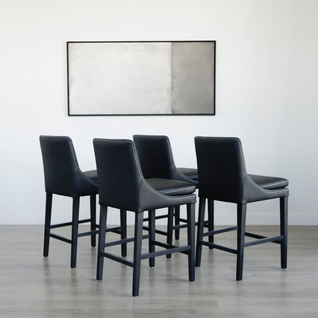 ensemble de tabourets comptoir en cuir végane noir avec coutures blanches et pieds en bois sombre.