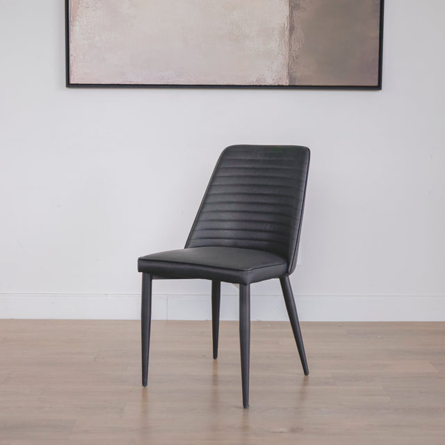 chaise moderne en simili cuir noir avec dossier a coutures horizontales et pieds en metal.