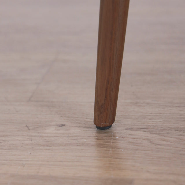 Image rapprochée d'une patte comportant un défaut d'un ensemble de deux chaises en cuir beige avec pattes en bois teinture noyer