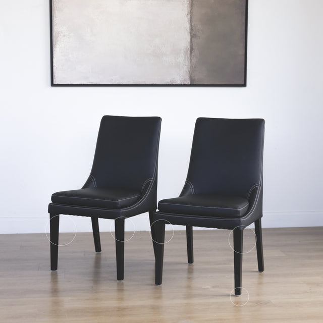 Ensemble de chaises moderne en cuir noir avec coutures blanches et pieds en bois sombre avec des cercles indiquant les défauts