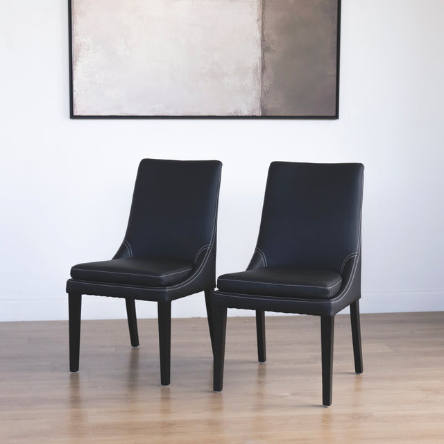 Ensemble de chaises moderne en cuir noir avec coutures blanches et pieds en bois sombre.