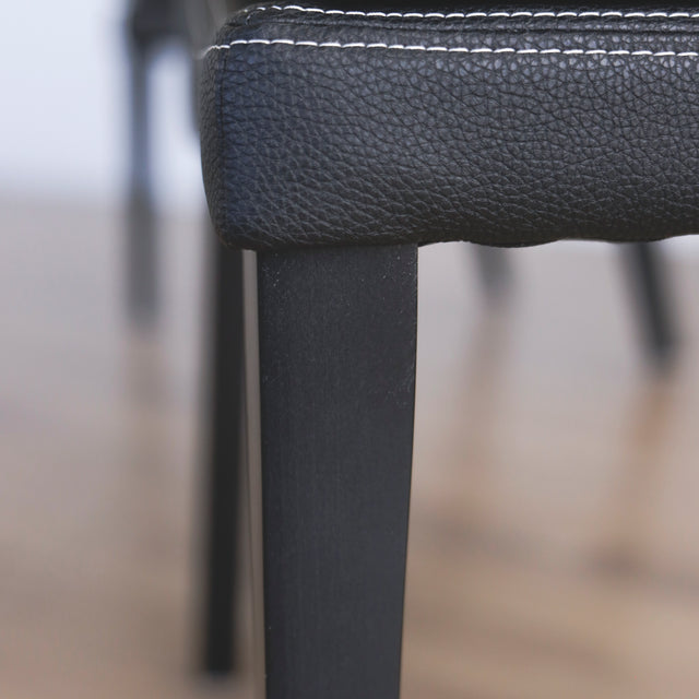 image rapprochée d'un ensemble de chaises moderne en cuir noir avec coutures blanches et pieds en bois sombre.