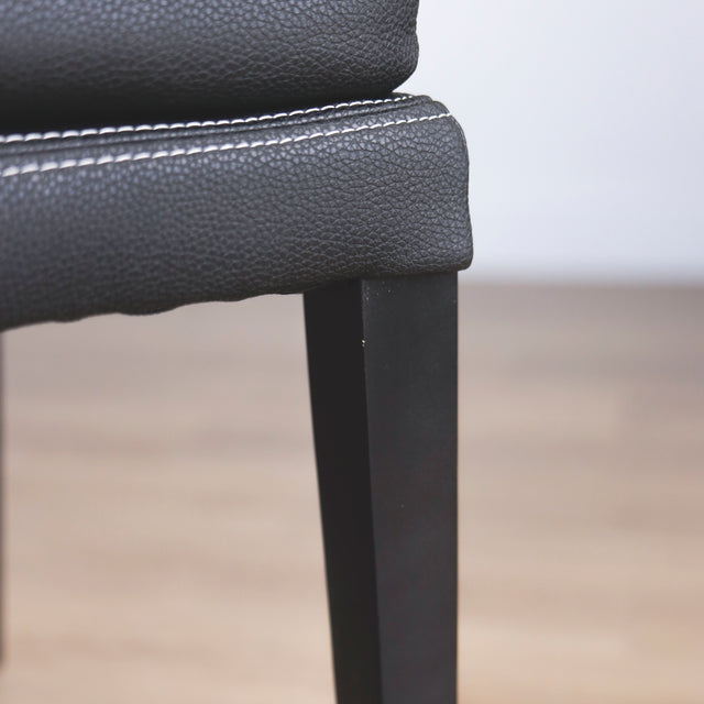 image rapprochée d'un ensemble de chaises moderne en cuir noir avec coutures blanches et pieds en bois sombre.