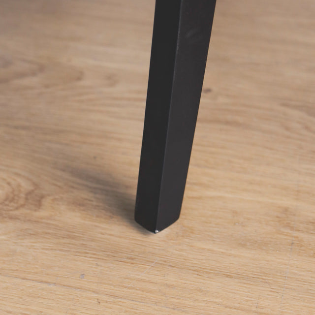 image rapprochée d'une patte d'un ensemble de chaises moderne en cuir noir avec coutures blanches et pieds en bois sombre.