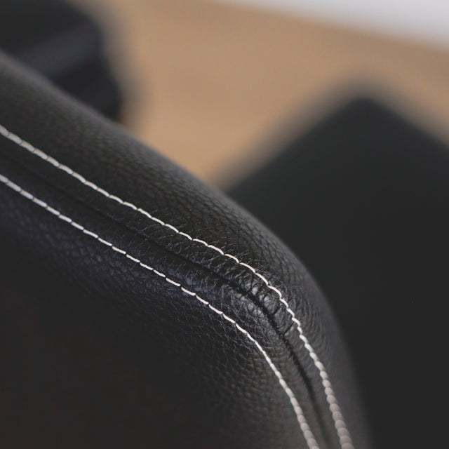 image rapprochée d'un ensemble de chaises moderne en cuir noir avec coutures blanches et pieds en bois sombre.