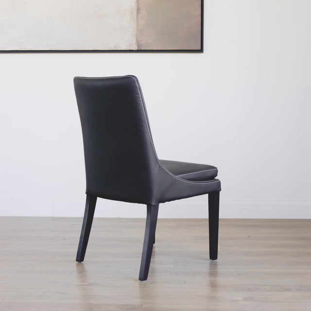 chaise moderne en cuir noir avec coutures blanches et pieds en bois sombre.
