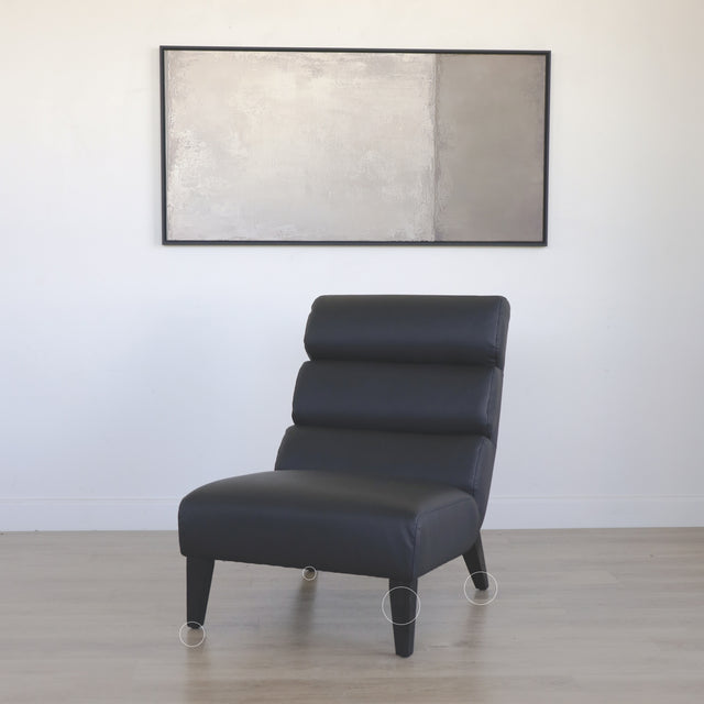 Fauteuil moderne en cuir noir avec dossier capitonne et pieds en bois fonce avec cercles indiquant les défauts.