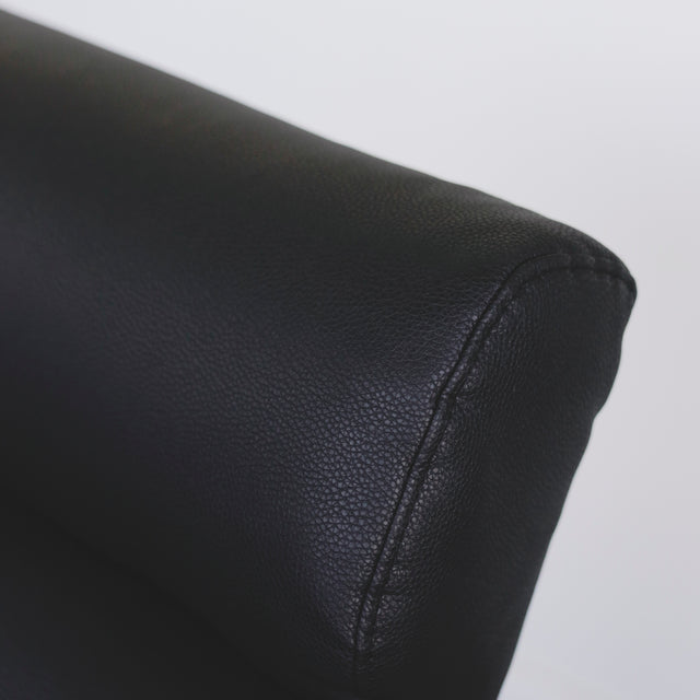 Image rapprochée d'un Fauteuil moderne en cuir noir avec dossier capitonne et pieds en bois fonce.